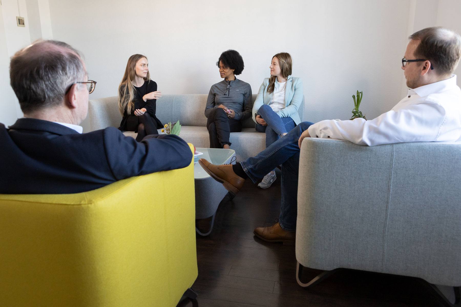 Indikationen in unserer Tagesklinik Fünf Personen sitzen und unterhalten sich in einem kleinen, hellen Büroraum, in dem ein Couchtisch und Topfpflanzen stehen.
